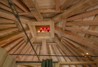 Houten balkenplafond met klein kleurrijk raam in boomhut 'Duiventoren' op Camping Les 3 Cantons, Frankrijk.
