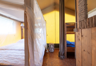 Interior de una tienda safari Woodlodge con cama doble, litera y decoración rústica de madera.