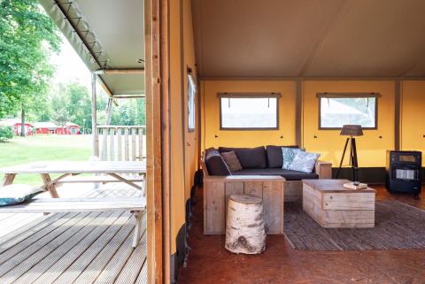Safari tent Woodlodge interior with rustic wooden furniture, cozy lounge area and outdoor picnic table view.