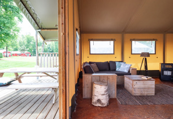 Intérieur de tente safari Woodlodge, meubles en bois rustiques, coin salon et table de pique-nique extérieure.