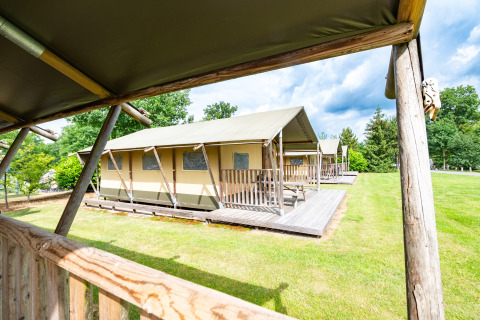 Safari tents at Veluwe campsite De Pampel in the Netherlands, viewed from a wooden porch on a sunny day.