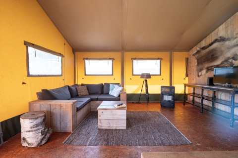 Salon du lodge safari Woodlodge au camping De Pampel Veluwe avec canapé, table basse et chauffage.