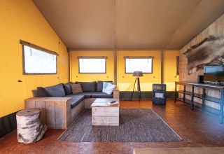 Salon du lodge safari Woodlodge au camping De Pampel Veluwe avec canapé, table basse et chauffage.