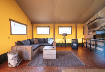 Soggiorno nella tenda safari Woodlodge al campeggio Veluwe De Pampel, arredamento accogliente e stufa.