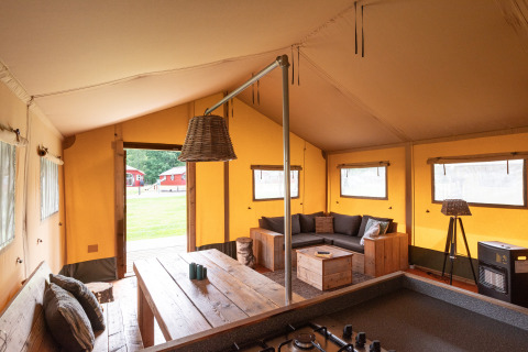 Vista interior de una tienda safari Woodlodge en el camping De Pampel con sofá y mesa de comedor.