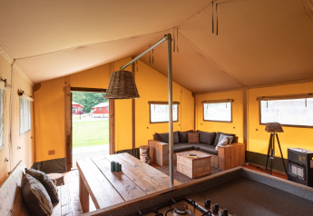 Vue intérieure d'une tente safari Woodlodge au camping De Pampel, avec canapé et grande table en bois.