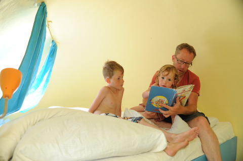 A father reads a book to his children inside the Dreaming in a Dragon's Egg pod at Veluwe campsite 't Schinkel.