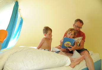 Ein Vater liest seinen Kindern ein Buch in einer Drachen-Ei-Pod auf dem Campingplatz 't Schinkel in den Niederlanden vor.