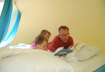 A man reads a book to two children on a bed inside a cozy pod at Veluwe campsite 't Schinkel in the Netherlands.