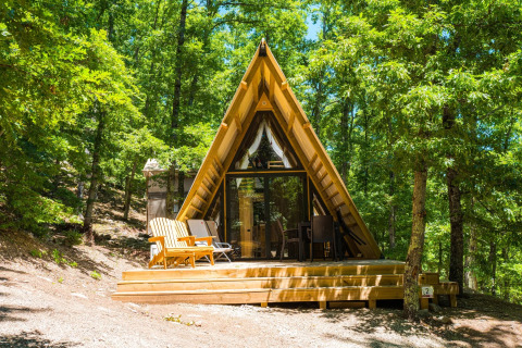 Een luxueuze A-frame lodge met houten terras tussen groene bomen, perfect om te ontspannen en van de natuur te genieten.