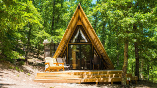 Eine luxuriöse A-Frame-Lodge mit Holzterrasse inmitten eines dichten Waldes, ideal zum Entspannen und Natur genießen.
