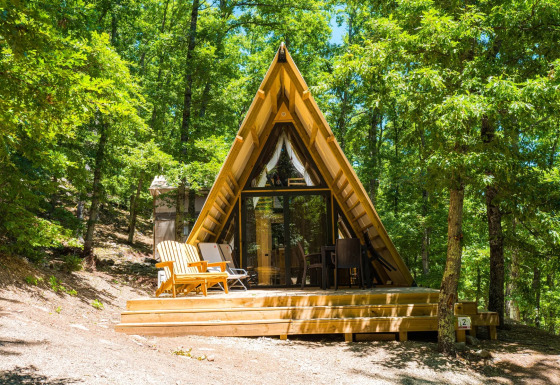 Een luxueuze A-frame lodge met houten terras tussen groene bomen, perfect om te ontspannen en van de natuur te genieten.
