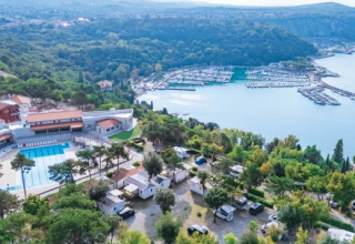 Aerial view of Village Mare Pineta campsite in Italy showing the pool, cabins, trees, and marina by the sea.