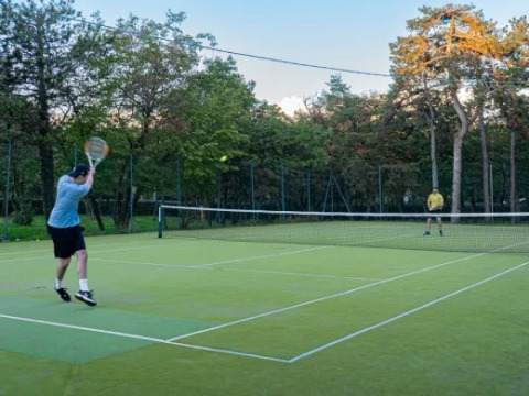 Due persone giocano a tennis su un campo all’aperto al campeggio Village Mare Pineta, Friuli-Venezia Giulia, Italia.