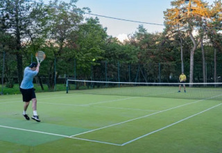 Two people playing tennis on an outdoor court surrounded by trees at Village Mare Pineta holiday park, Italy.