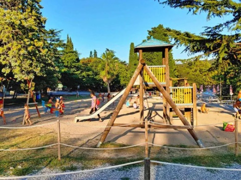Children playing on a playground with slides and wooden structures at Village Mare Pineta campsite, Italy.