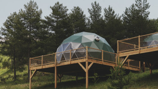 Cupola geodetica 'Domo' Family su piattaforma in legno al Wecamp Pedraforca, Spagna, circondata da alberi.