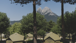 Safari tenten op een camping met uitzicht op een indrukwekkende bergtop tussen groene bomen.