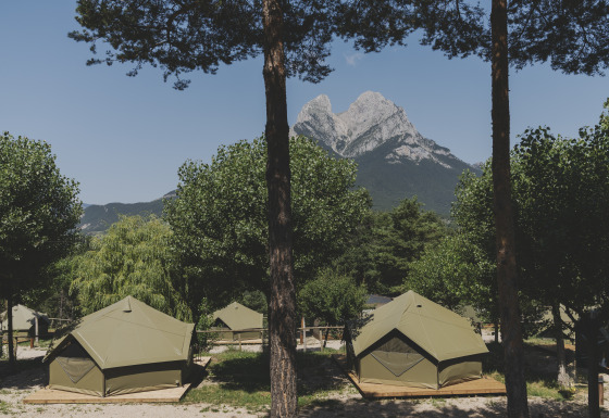 Safaritenten op houten platforms op een camping, met op de achtergrond een imposante bergtop.