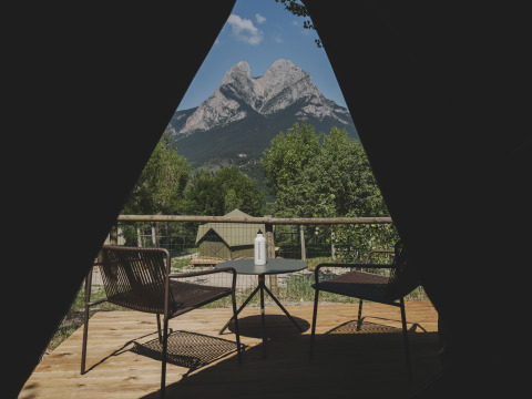 Gezicht vanuit de Bell Tent op Wecamp Pedraforca, Spanje, met een terras, stoelen en bergen op de achtergrond.
