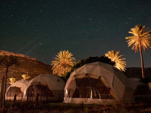 Cúpulas geodésicas y palmeras bajo un cielo estrellado en Wecamp Cabo de Gata, Andalucía, España de noche.