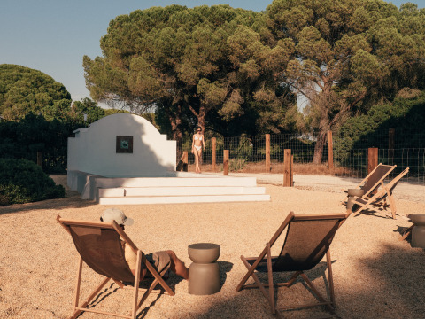 Udendørs afslapningsområde på Wecamp Cádiz i Andalusien med liggestole, træer og en person ved poolen.