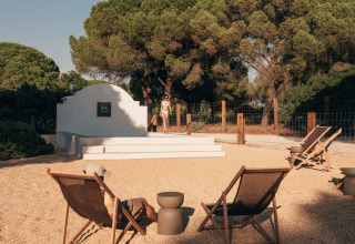 Buiten ontspanningsruimte aan Wecamp Cádiz in Andalusië met ligstoelen, bomen en iemand bij het zwembad.