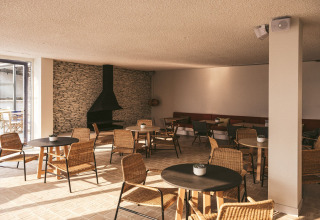 Solrigt loungeområde i Wecamp Cadaqués, Catalonien, med kurvestole, borde og stenpejsebagvæg.