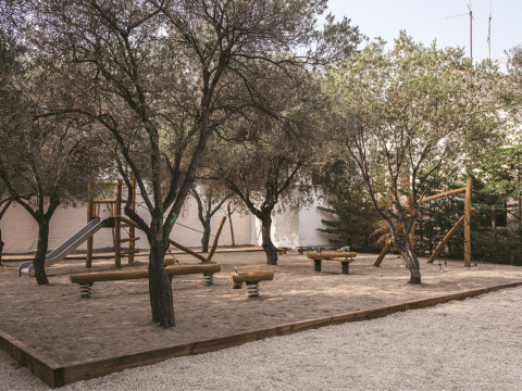 Speeltuin met houten toestellen en glijbaan onder bomen bij Wecamp Cadaqués vakantiepark in Catalonië, Spanje.