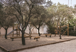Parco giochi con attrezzature in legno e scivolo sotto gli alberi al Wecamp Cadaqués, Catalogna, Spagna.