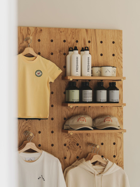 Display with clothing, water bottles, caps, and toiletries on a wooden pegboard at Wecamp Jávea in Valencia, Spain.