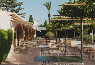Außenterrasse mit modernen Tischen und Stühlen im grünen Garten von Wecamp Jávea in Valencia, Spanien.