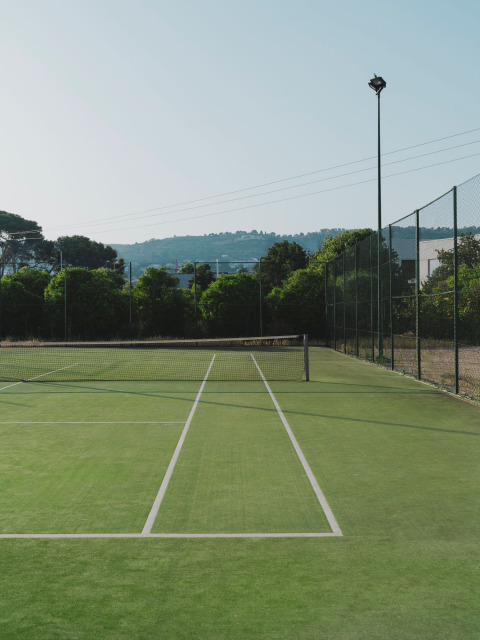Buiten tennisbaan met groen gras en net, omringd door bomen bij Wecamp Jávea, Valencia, Spanje.