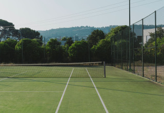Buiten tennisbaan met groen gras en net, omringd door bomen bij Wecamp Jávea, Valencia, Spanje.