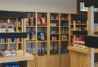 Interieur van een klein winkeltje met houten schappen vol snacks bij Wecamp Pirineos in Aragón, Spanje.
