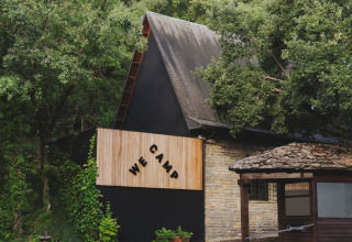 A-vormig gebouw bij de ingang van Wecamp Pirineos vakantiepark in Aragón, Spanje, tussen bomen.