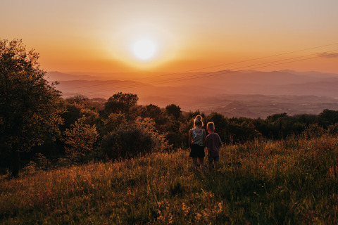 Two people watching a scenic sunset from a grassy field at Campsite Lucherino holiday park, Tuscany, Italy.