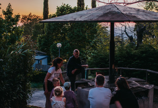 Family and friends gather around an outdoor barbecue at Campsite Lucherino, Tuscany, Italy at sunset.