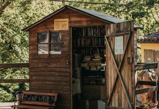 Une petite cabane en bois remplie de livres au camping Lucherino en Toscane, Italie, entourée d’arbres.