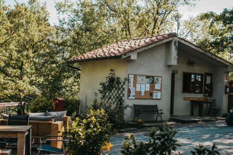 Vue extérieure d’un bâtiment avec panneau d’affichage et bancs au camping Lucherino en Toscane, Italie.