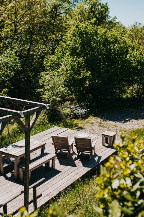Terrasse en bois avec chaises au camping Lucherino en Toscane, Italie, entourée de verdure et d’arbres.
