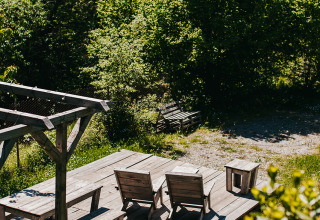 Wooden terrace with chairs and a table at Campsite Lucherino holiday park in Tuscany, Italy, surrounded by trees.