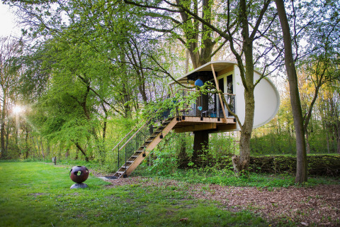 Modern treehouse suite at Buytenplaets Suydersee, Netherlands, surrounded by lush green forest trees.