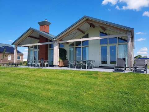 Modernes Glamping-Ferienhaus mit großen Fenstern, Terrasse und grüner Wiese unter blauem Himmel.