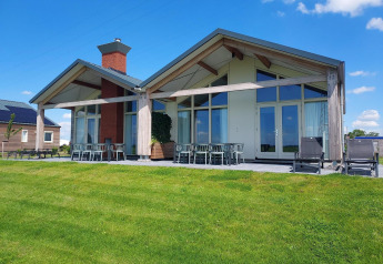 Alojamiento glamping moderno con grandes ventanales, patio y césped bajo un cielo azul y nubes blancas.