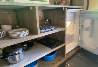 Offenes Küchenregal im Safarizelt mit Geschirr, Töpfen und offenem Kühlschrank in den Niederlanden.