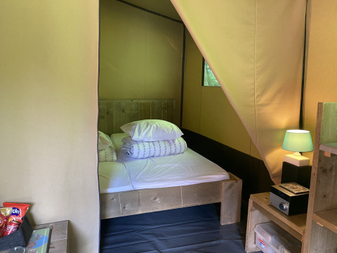 Innenaufnahme eines Safari-Zelts mit Doppelbett, Nachttisch, Lampe und Snacks bei Buytenplaets Suydersee.