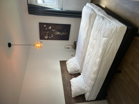 Schlafzimmer mit Doppelbett, heller Bettwäsche, Wandkunst und Lampe im Sea bass Chalet, Zeeland, Niederlande.