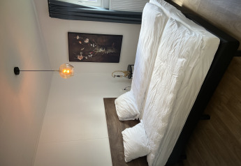 Bedroom with double bed, white bedding, wall art, lamp and window in Sea bass chalet, Holiday Park de Zeeuwse Parel.