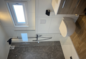 Modern bathroom with shower, wall-mounted toilet and window in Sea bass chalet at Holiday Park de Zeeuwse Parel.